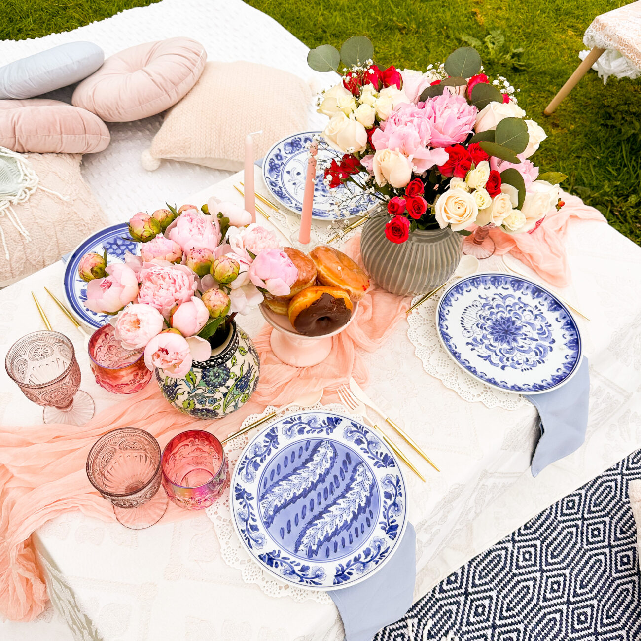 Luxurious park picnic setup with peony centerpiece, candles, and donuts ready to be savored